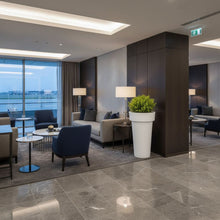 Load image into Gallery viewer, Extra tall 1metre tall planter called 'The Skinny' in Modern airport hotel lobby with seating area, large windows,